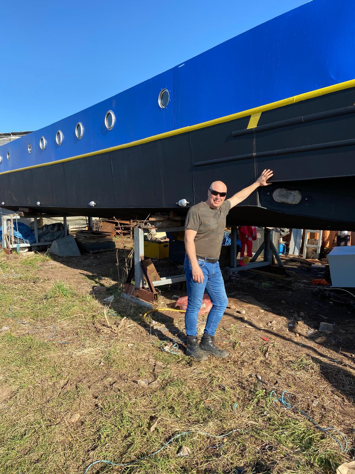 Mike Foulkes beside the steel narrowboat he built, up on stands in the yard