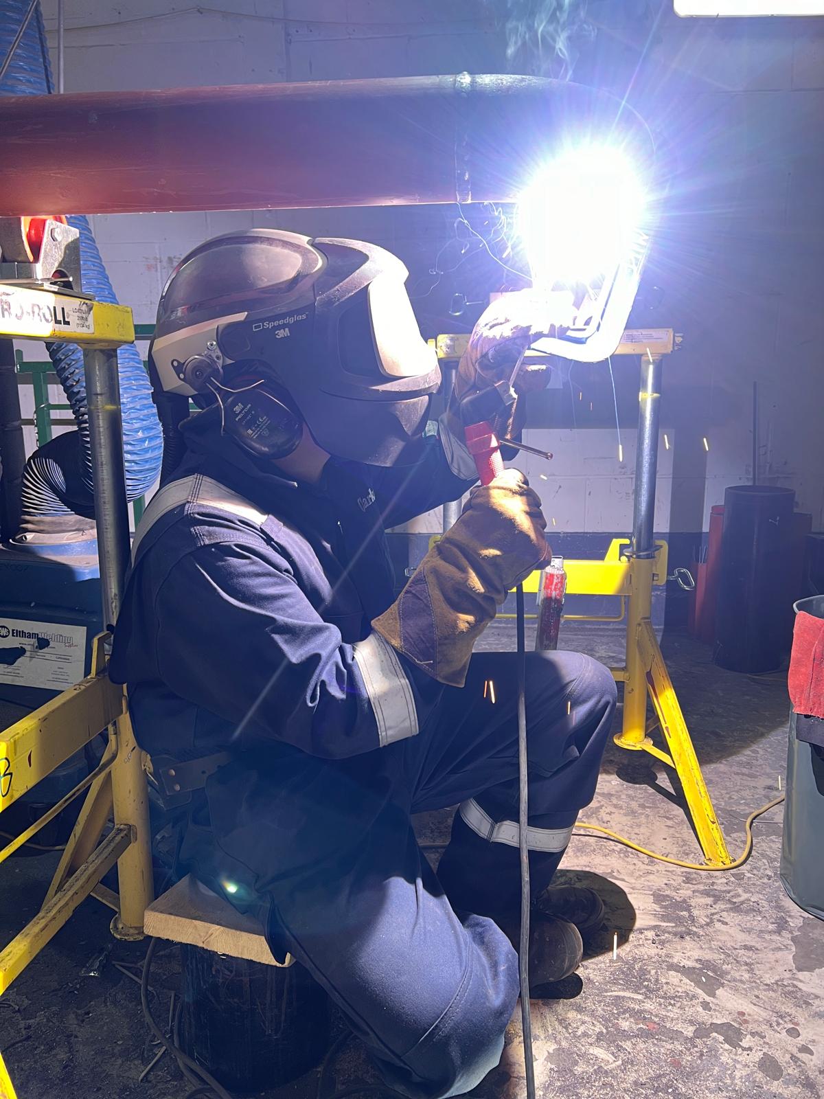 Mike welding inside a confined site bay, sparks falling from the arc